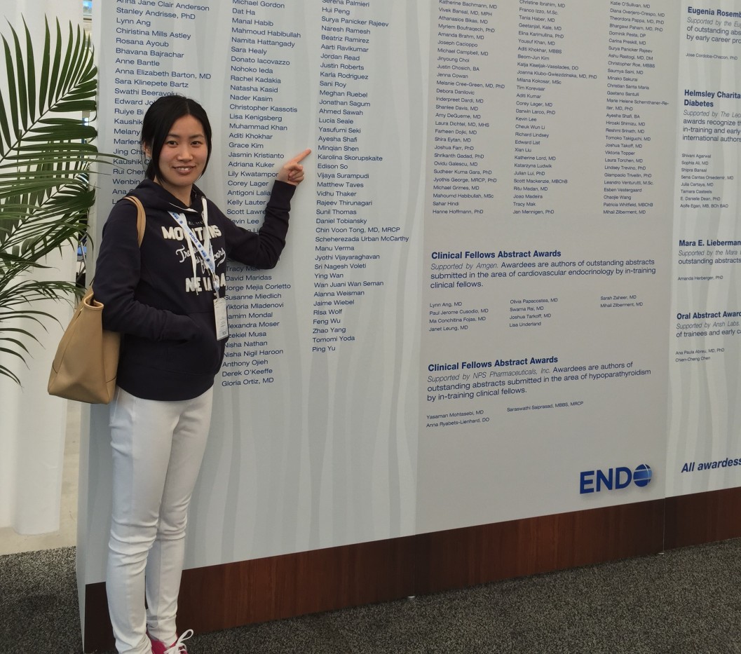 A woman stands in front of a very large poster. She points to her name -- Minqian Shen -- within a long list of names. Visible text: ENDO. 2015 Abstract Awards and Travel Grants. Early Career Forum Travel Awards. Supported by the Endocrine Society. These application-based travel awards are presented to graduate students, medical students, postdoctoral fellows, and clinical fellows in endocrinology. 125 travel awards supported by the Society; 2 additional travel awards supported by Women in Endocrinology.